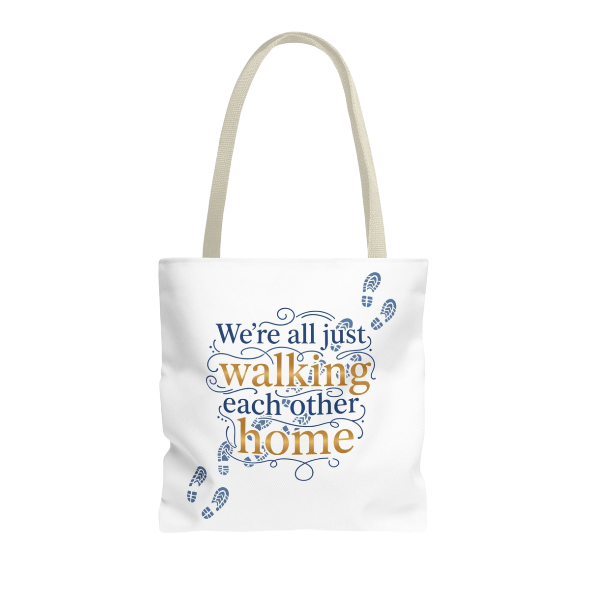 A white canvas tote bag with beige shoulder straps, featuring a printed quote that reads 'We're all just walking each other home' in blue and orange lettering, accented with blue footprints, on a plain white background.