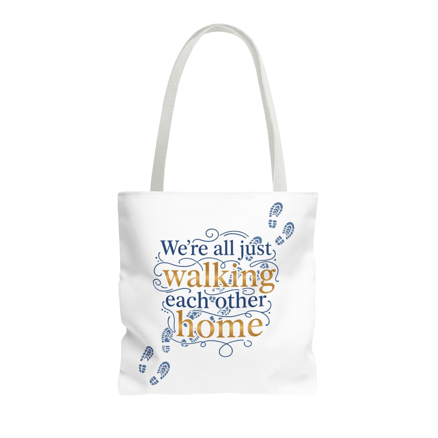 A white canvas tote bag with white shoulder straps, featuring a printed design on the front. The design displays the phrase 'We're all just walking each other home' in navy blue and mustard yellow lettering, accented with blue baby footprints and decorative swirls.