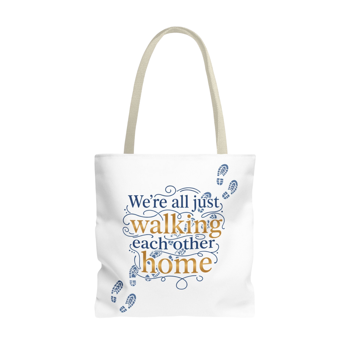A white canvas tote bag with beige handles, featuring a printed graphic on the front that reads 'We're all just walking each other home' in navy blue and mustard yellow lettering, accented with small blue footprint illustrations.