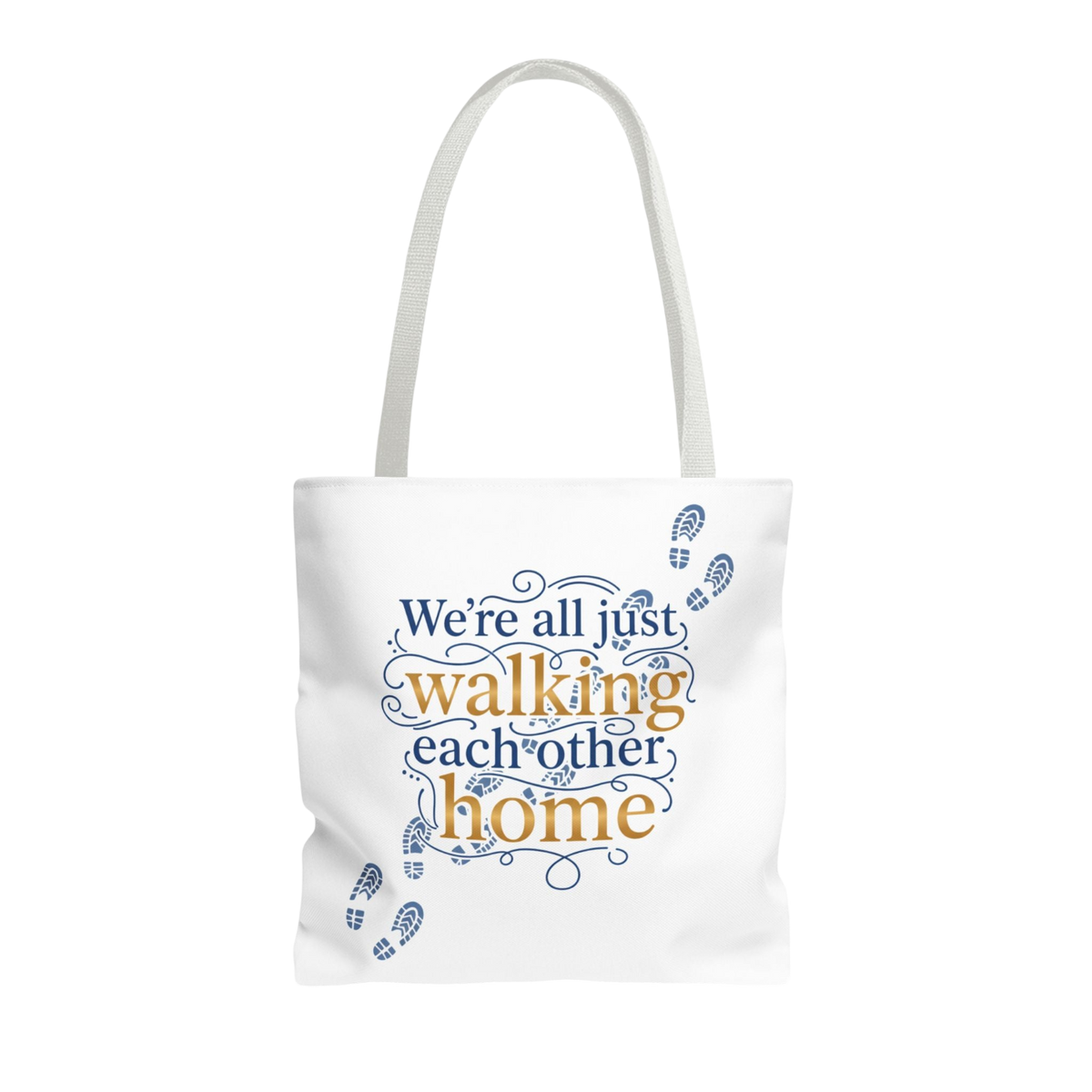 A white canvas tote bag with white shoulder straps, featuring a printed design on the front. The design displays the phrase 'We're all just walking each other home' in navy blue and mustard yellow lettering, accented with blue baby footprints and decorative swirls.