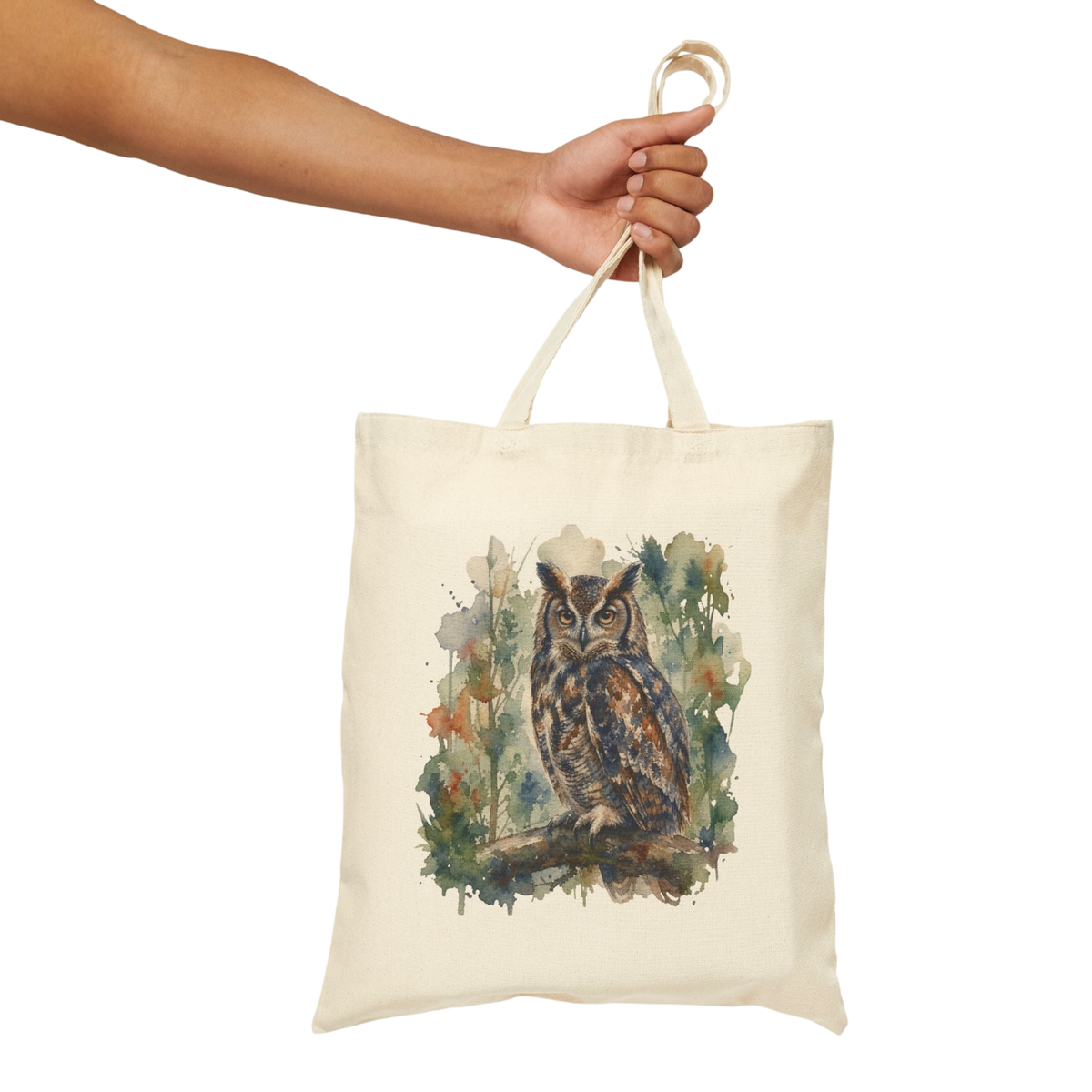 A cream canvas tote bag with a watercolor-style owl illustration on the front, held by a person's arm against a plain white background.