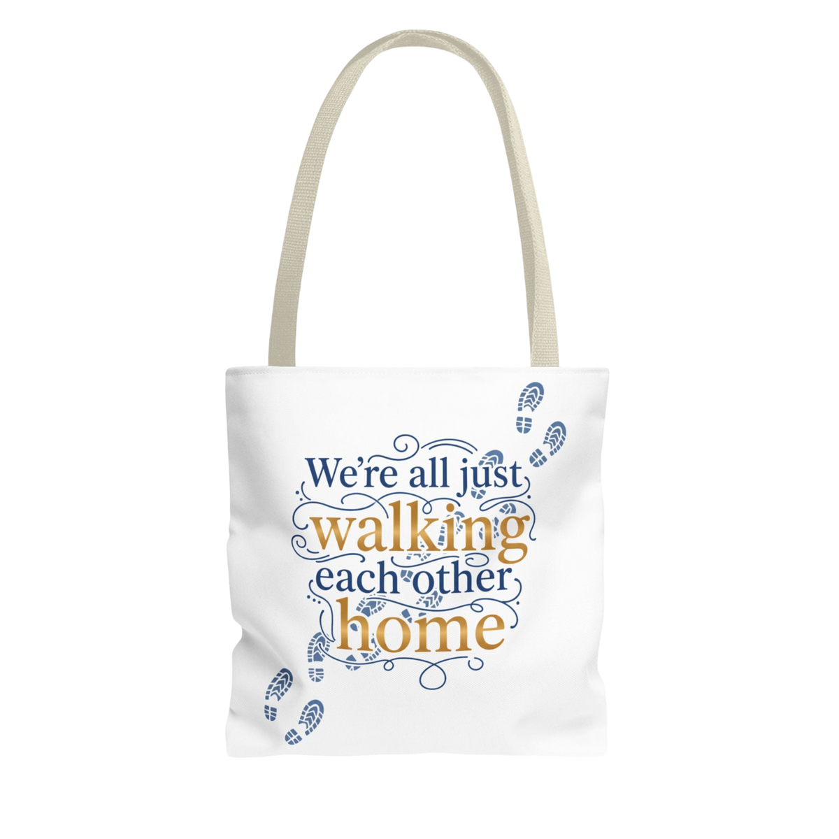 A white canvas tote bag with beige shoulder straps, featuring the printed phrase 'We're all just walking each other home' in blue and gold lettering with blue footprint illustrations.