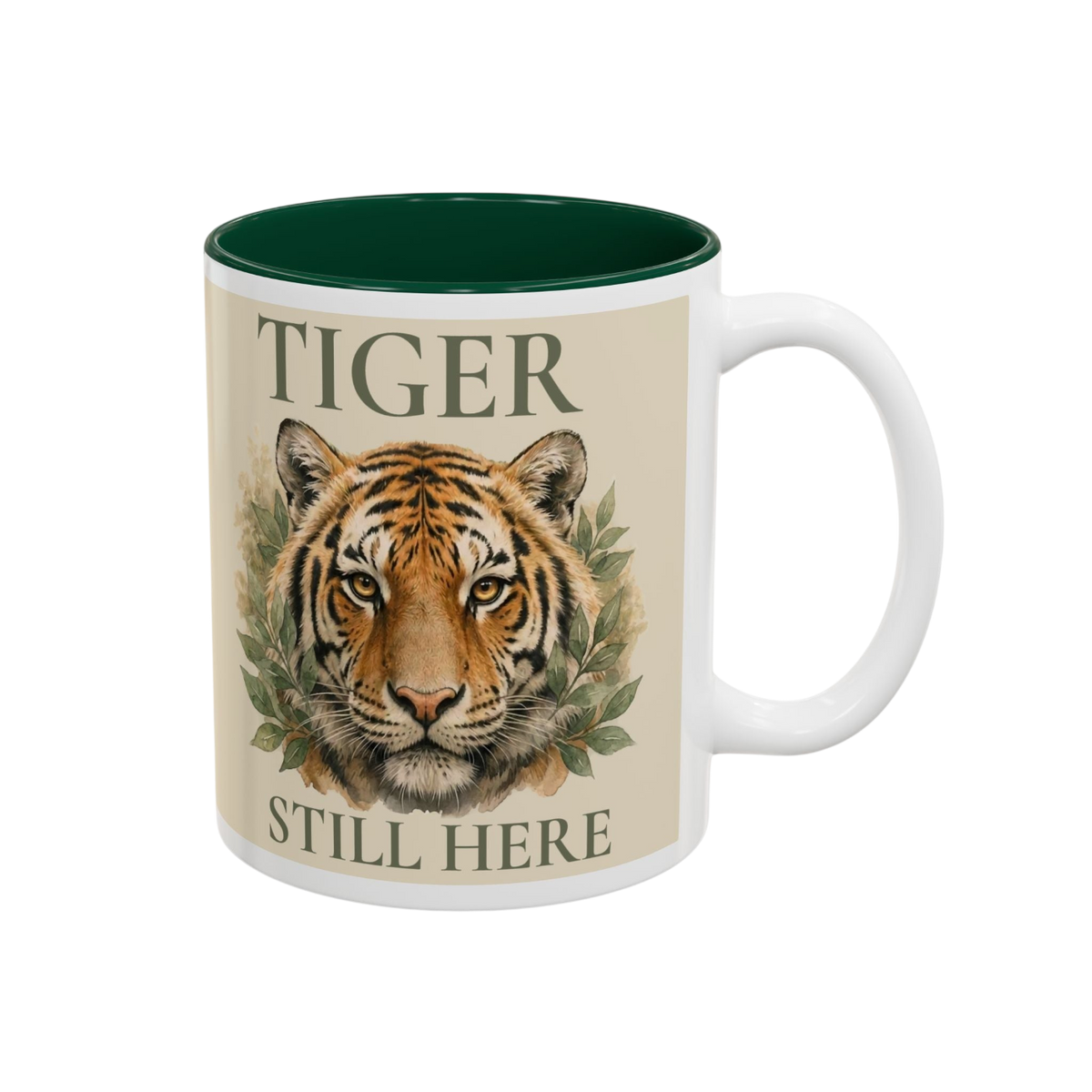 A white ceramic mug with a dark green interior, featuring a printed design of a tiger's face framed by green leaves, with the words 'TIGER' above and 'STILL HERE' below, on a plain white background.